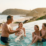 A pre-retiree couple in their 50s and their two teenage children laughing and splashing in an infinity pool overlooking the ocean and Point Perry at Coolum Beach.